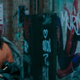 Morbius, in a orange jumpsuit and gray robe, walks past a graffitied picture of Spider-Man in an alley.